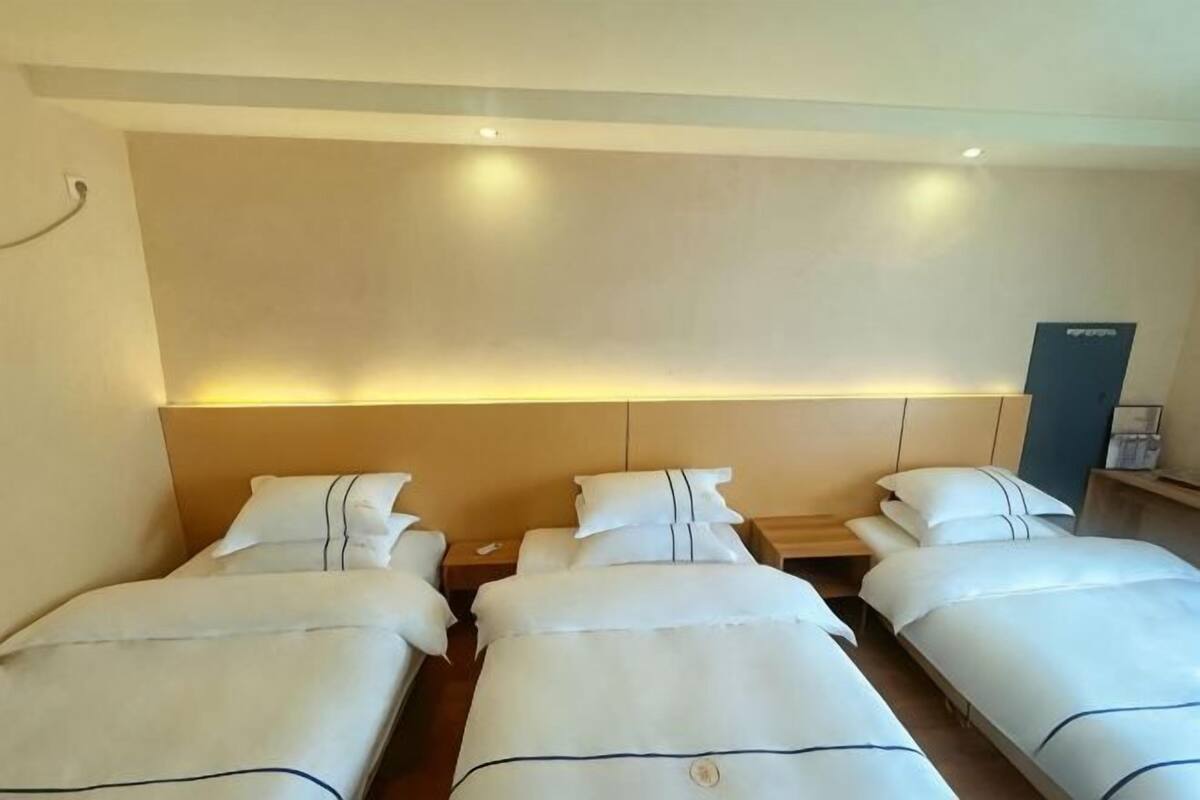 A hotel room with two single beds, a large headboard, and a nightstand with a lamp.