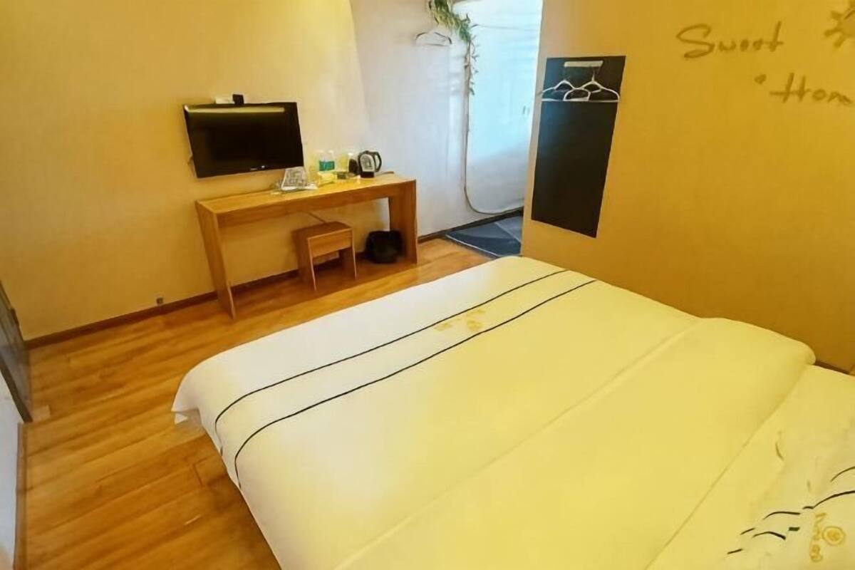 A hotel room with a bed, a desk with a flat-screen TV, a small chair, and a wall-mounted TV.