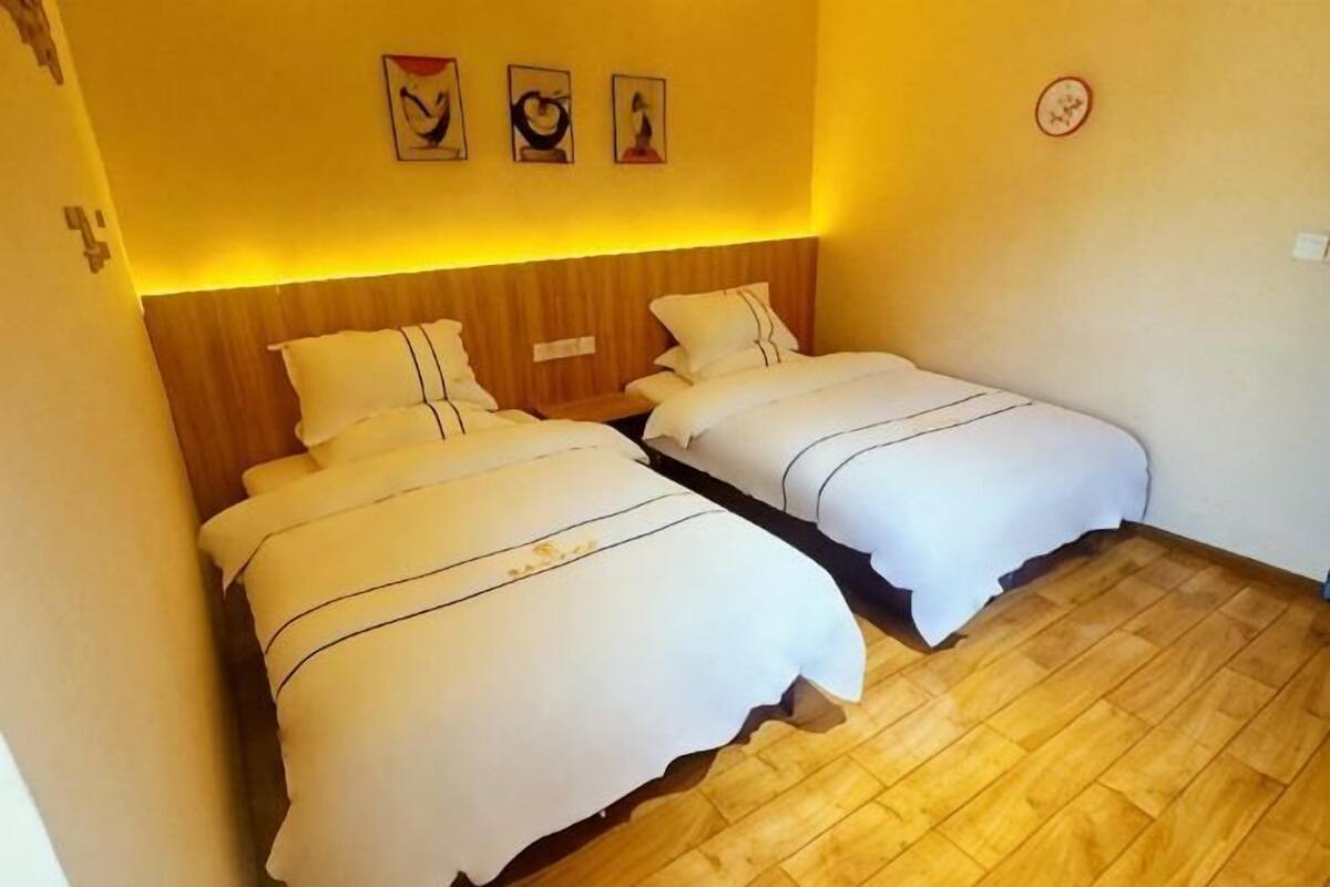 A room with two beds, wooden flooring, and wall-mounted artwork.