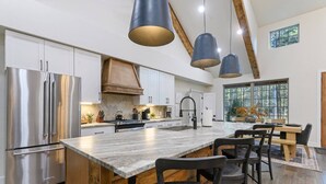 Una cucina moderna con elettrodomestici in acciaio inossidabile, una grande isola con sgabelli da bar e illuminazione a sospensione.
