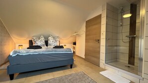 Ein Schlafzimmer mit Bett, Nachttisch, Dusche und Holztür.
