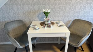 Ein Essbereich mit einem weißen Tisch, gedeckt für zwei Personen, mit Geschirr mit Blumenmuster und einer Vase mit weißen Blumen.