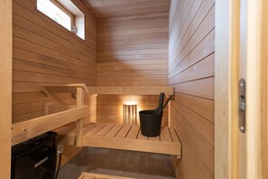 A wooden sauna with benches, a black bucket, and a small light fixture. - Forenom Serviced Apts Turku Mälikkälä (Turku)