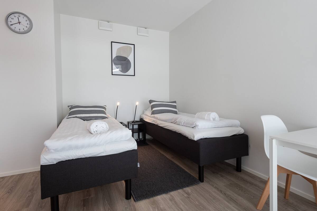 Ein modernes Schlafzimmer mit zwei Einzelbetten, einem weißen Schreibtisch und einer Uhr an der Wand.
