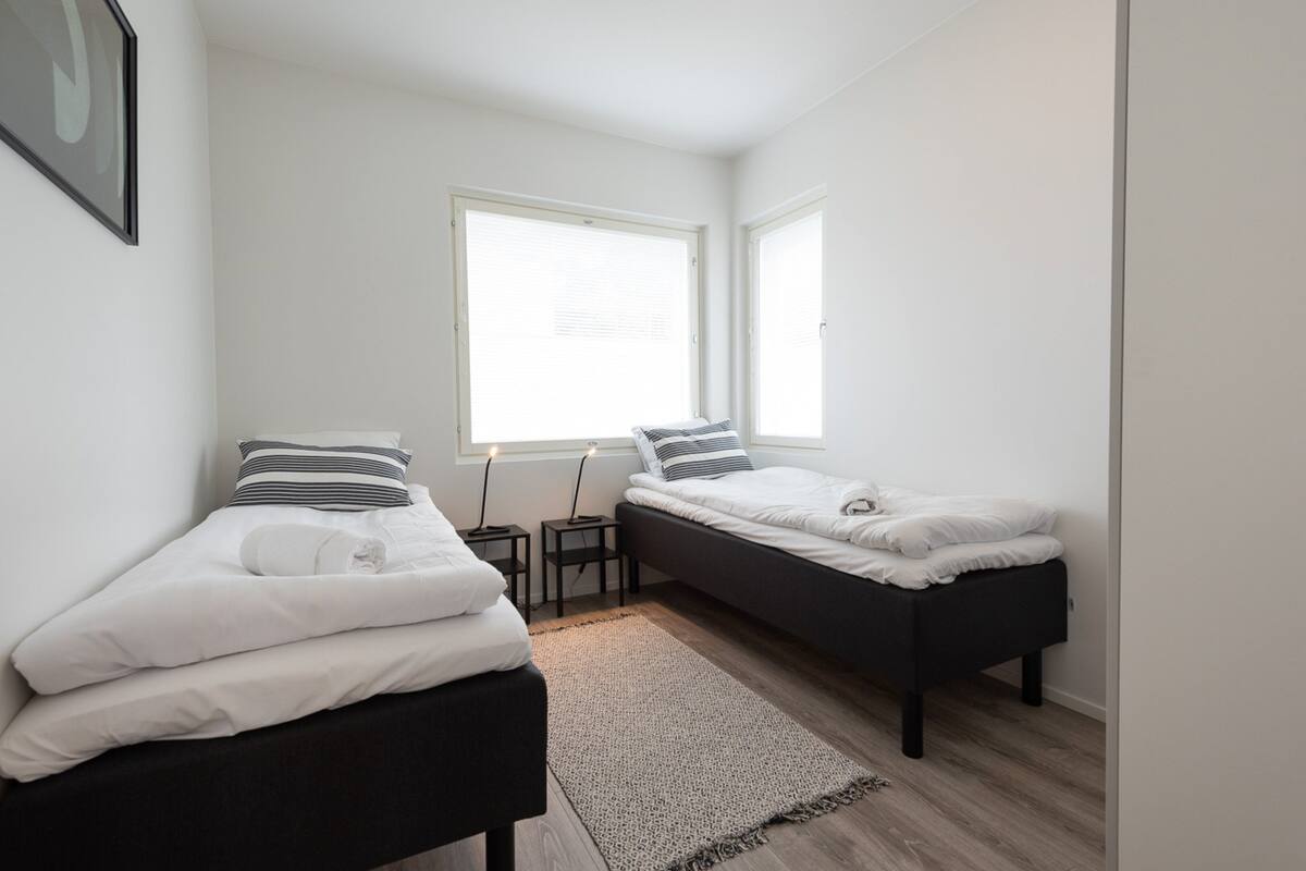 Ein kleines, modernes Schlafzimmer mit zwei Einzelbetten, einem großen Fenster und einem Nachttisch mit Lampe.