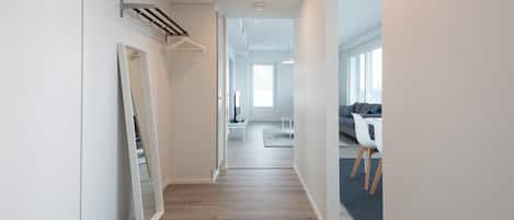 A modern hallway with a wooden floor, a white door, and a hanging coat rack.