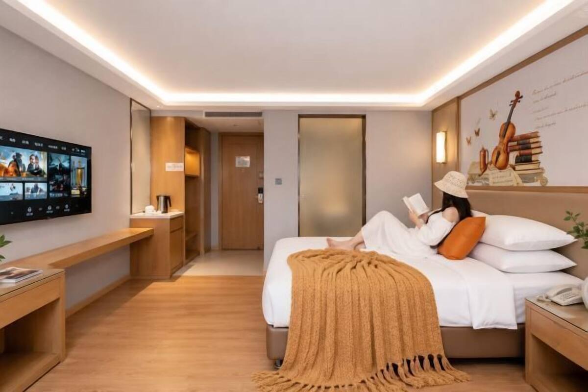 A modern hotel room with a bed, bedside table, TV, and a wall-mounted artwork.