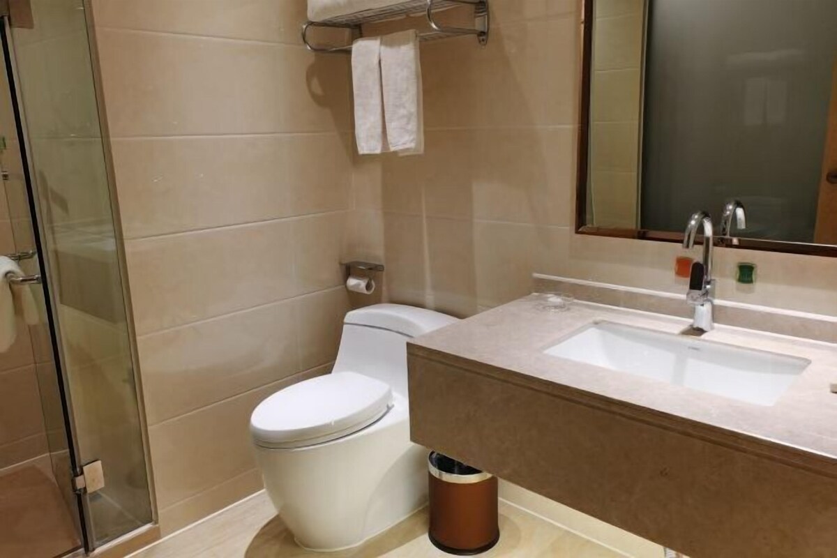 A modern bathroom with a glass shower enclosure, a white toilet, a beige sink with a mirror, and a trash bin.