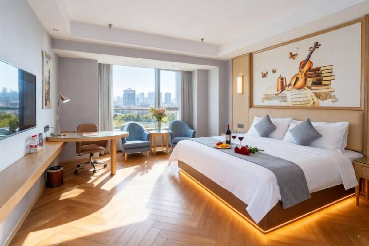 A modern hotel room with a large bed, a desk, a chair, and a city view.