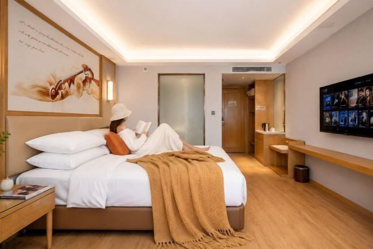 A hotel room with a bed, bedside table, reading lamp, and a wall-mounted TV.