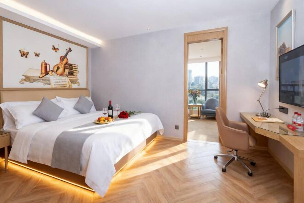 A hotel room with a bed, a desk, a chair, a TV, and a painting on the wall.