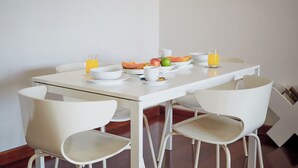 Ein Esstisch mit weißen Stühlen, eine Fruchtschale und zwei Gläser Orangensaft.