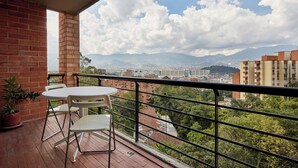 Ein Balkon mit Tisch und Stühlen mit Blick auf eine Stadtlandschaft, in der Ferne Berge.