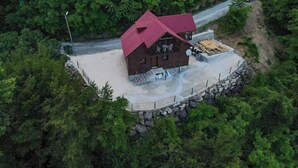 A cabin with a red roof surrounded by dense forest, a paved driveway, and a stone wall. - DIAMOND TREE HOUSE (Maçka)