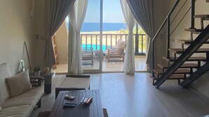 A spacious living area with a sofa, coffee table, and a view of the balcony and pool.
