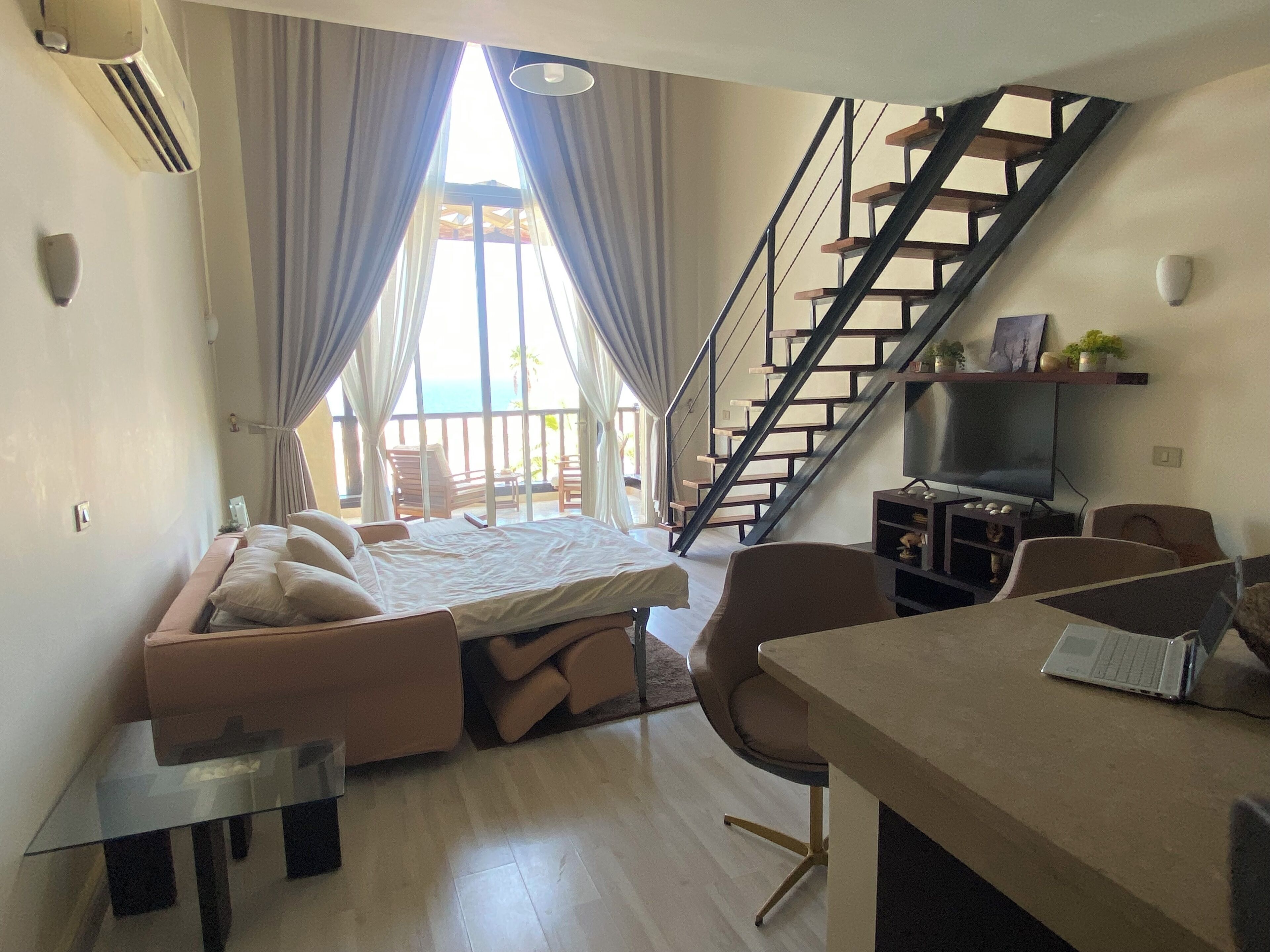 A modern bedroom with a bed, a desk, a chair, a TV, and a staircase.