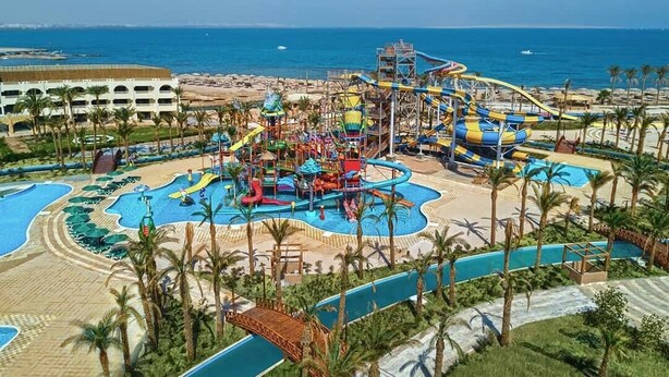 A water park with multiple slides and pools, surrounded by palm trees and a beach.