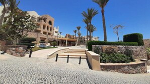 A hotel entrance with a stone pathway leading to a building with multiple balconies and palm trees.