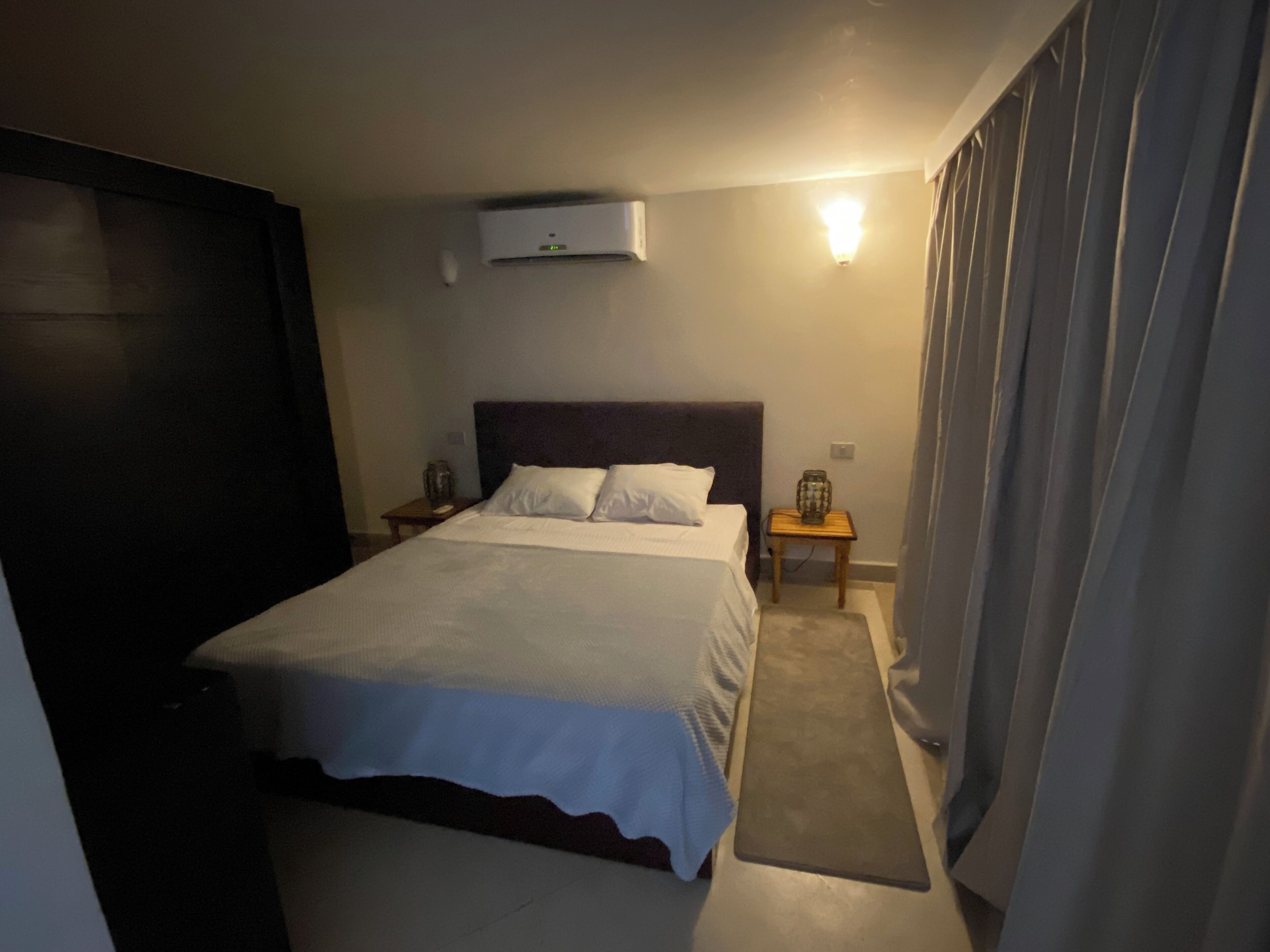 Ein Hotelzimmer mit einem Bett, einem Nachttisch, einer Lampe und einer Wandklimaanlage.