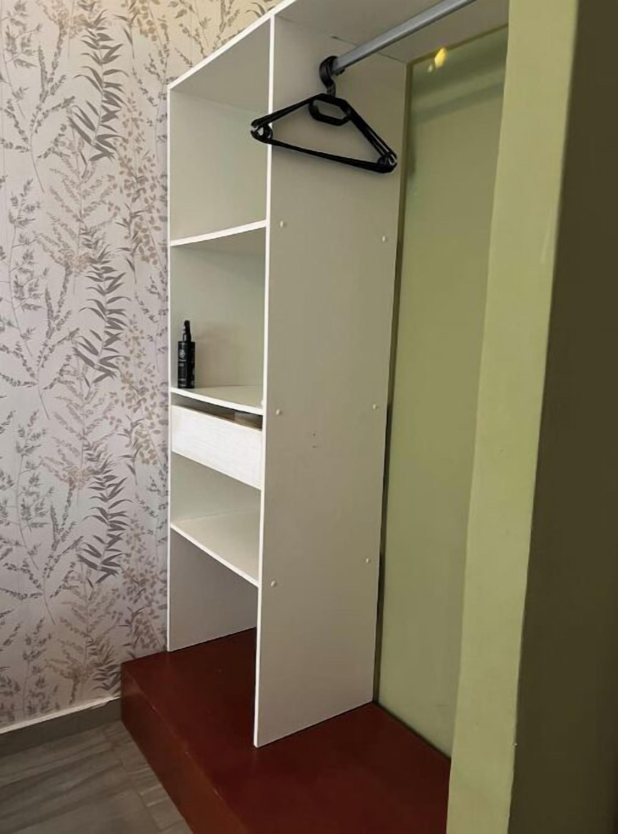 A walk-in closet with white shelves and a black hanger.