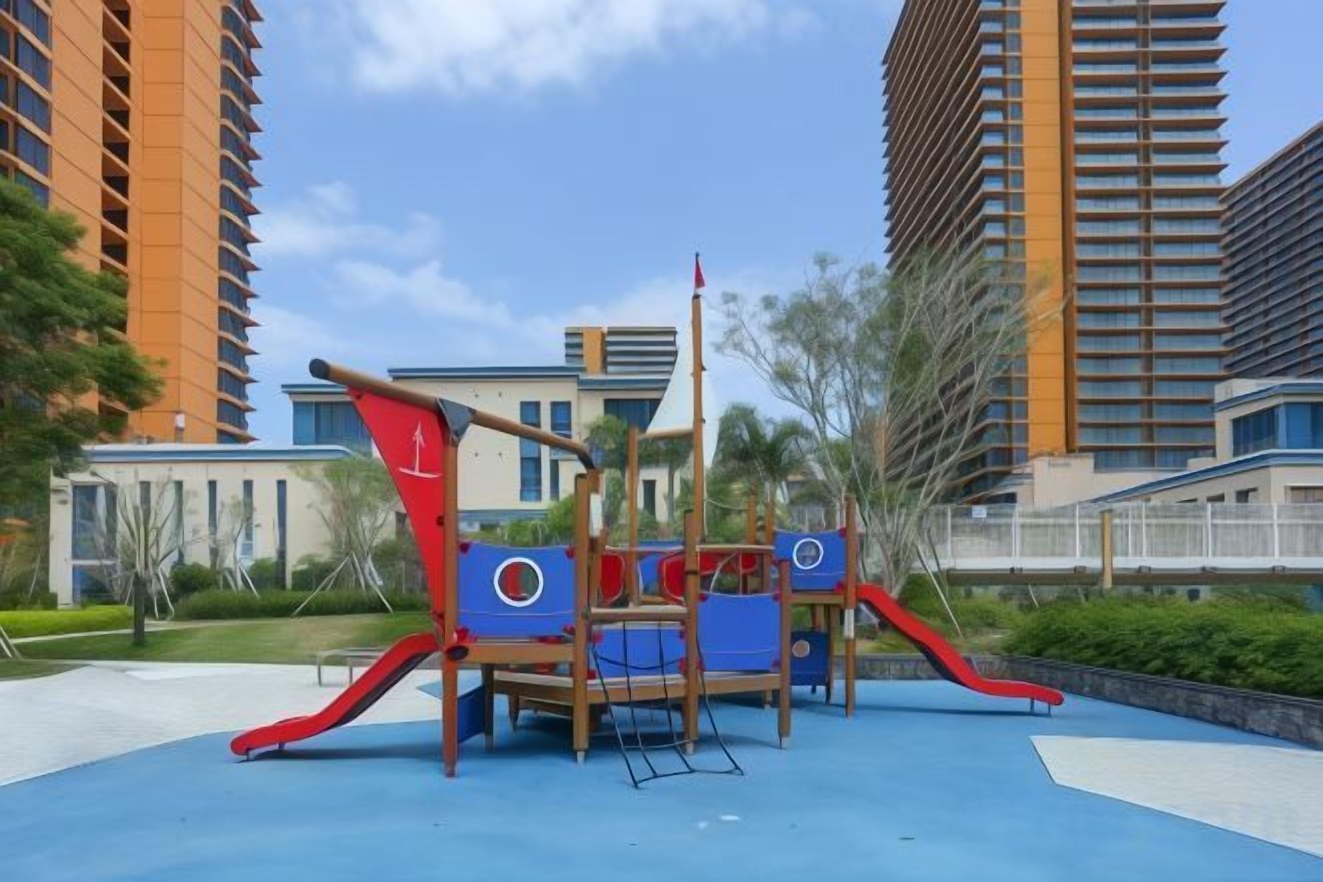 Un parque infantil con toboganes y estructuras para escalar, rodeado de edificios y vegetación.
