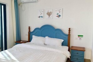 Ein Schlafzimmer mit blauem Kopfteil, weißer Bettwäsche, einem kleinen Nachttisch und einer Wand-Klimaanlage.