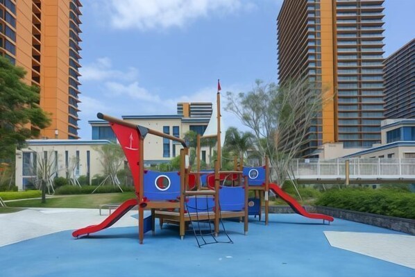 A playground with a slide and climbing structures, surrounded by tall residential buildings.