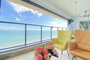 A balcony with a view of the sea, two chairs, and a flower arrangement. - Happy Bay Holiday Apartment (Huidong)