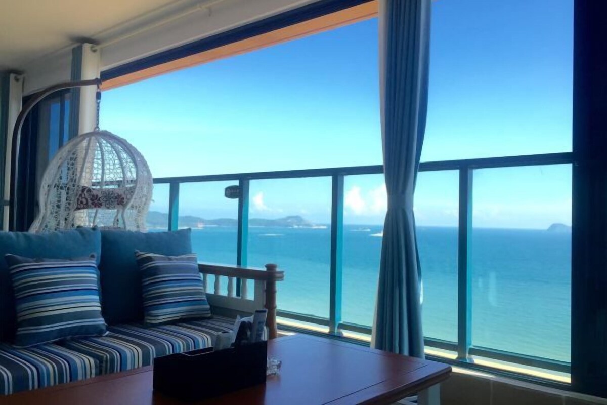 A balcony with a view of the ocean, a hanging chair, and a sofa with striped cushions.
