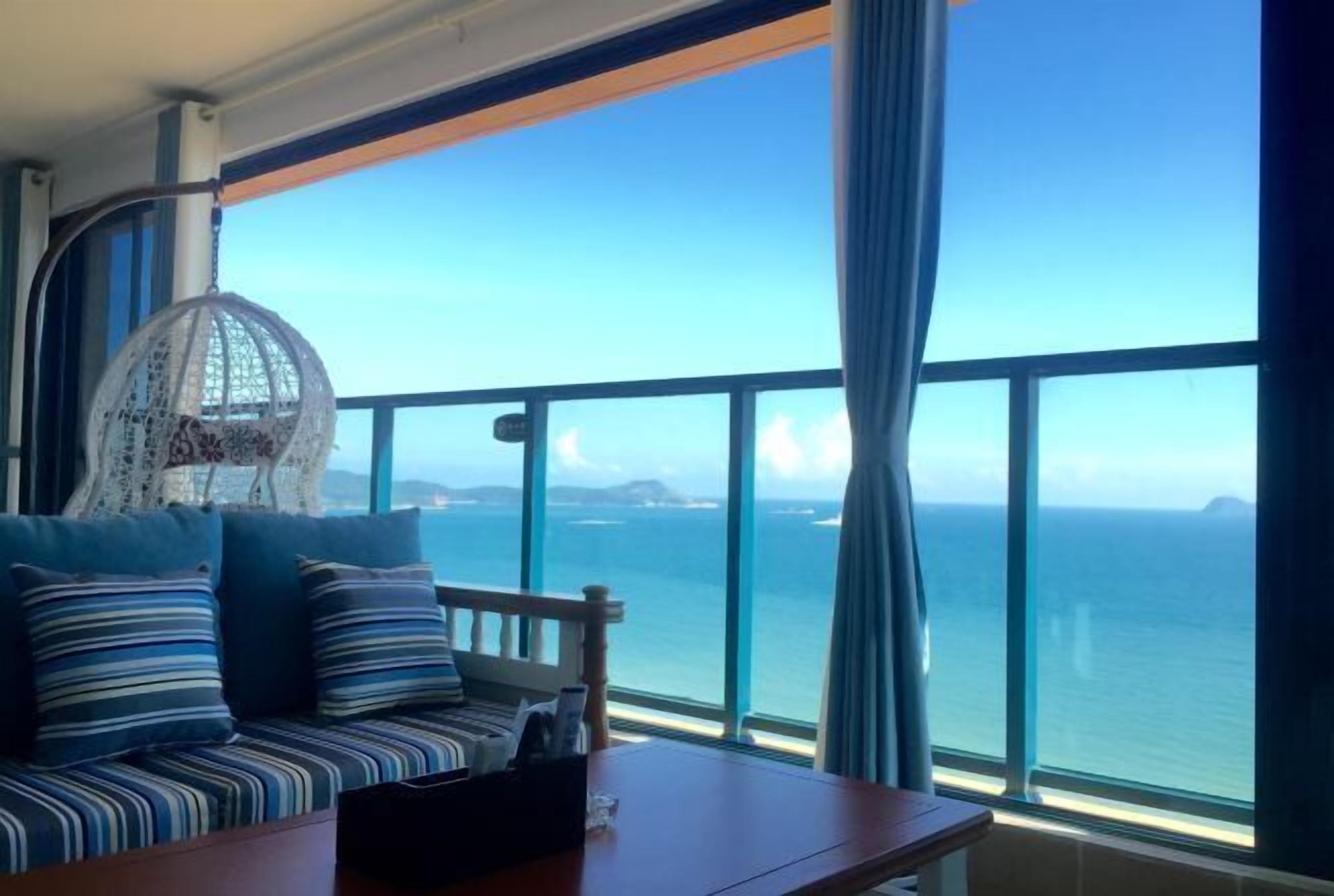 Uma varanda com vista para o oceano, uma cadeira suspensa e um sofá com almofadas listradas.
