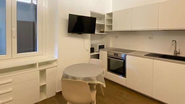 Une cuisine moderne avec des meubles blancs, un four encastré, un four à micro-ondes et une grande fenêtre.