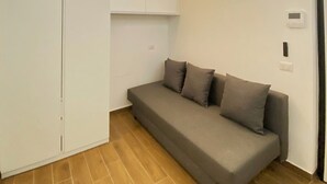 Une petite pièce moderne avec un canapé gris, une armoire blanche et un sol carrelé marron.
