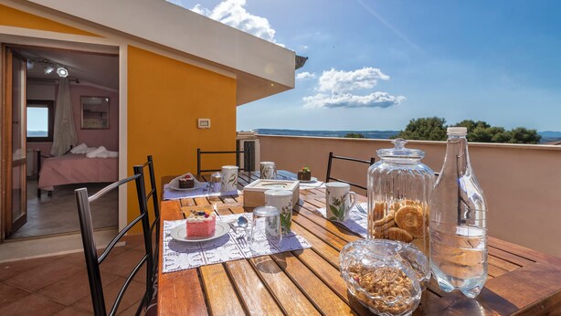 A dining table set outdoors with a view of the sea, a bed inside, and a yellow wall. - Casa Clara Uri in the Nuraghe of Santa Cadrina a short distance from the beaches (Uri)