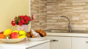 A kitchen counter with a bowl of fruits, a vase of red flowers, and a plate of pastries. - Casa Clara Uri in the Nuraghe of Santa Cadrina a short distance from the beaches (Uri)