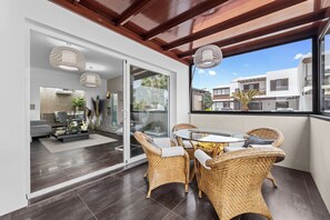 A modern living room with a glass door leading to a kitchen, wicker furniture, and a view of neighboring buildings. - Casa Lyrata (Costa Teguise)
