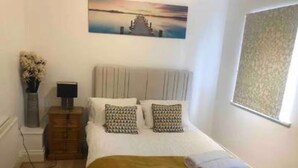 A bedroom with a bed, a nightstand, a lamp, a painting, and a window. - Stunning 3-bed House in Bristol (Bristol)