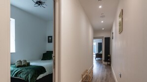 A hallway leading to a bedroom with a bed, a bedside table, and a window. - Central Cardiff Luxury Exceptional 2-Bed Apartment in the City Centre (Cardiff)