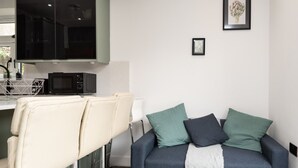A compact living space with a kitchenette, a sofa with cushions, and a framed artwork on the wall. - Central Cardiff Luxury Exceptional 2-Bed Apartment in the City Centre (Cardiff)