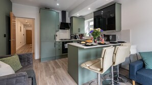A modern kitchen with a central island, bar stools, and a dining area with a table and chairs. - Central Cardiff Luxury Exceptional 2-Bed Apartment in the City Centre (Cardiff)