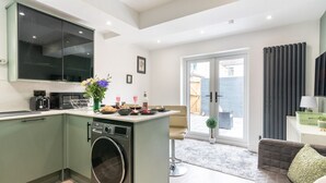 A modern kitchen with a washing machine, a dining area with a table and chairs, and a sliding glass door leading to a balcony. - Central Cardiff Luxury Exceptional 2-Bed Apartment in the City Centre (Cardiff)