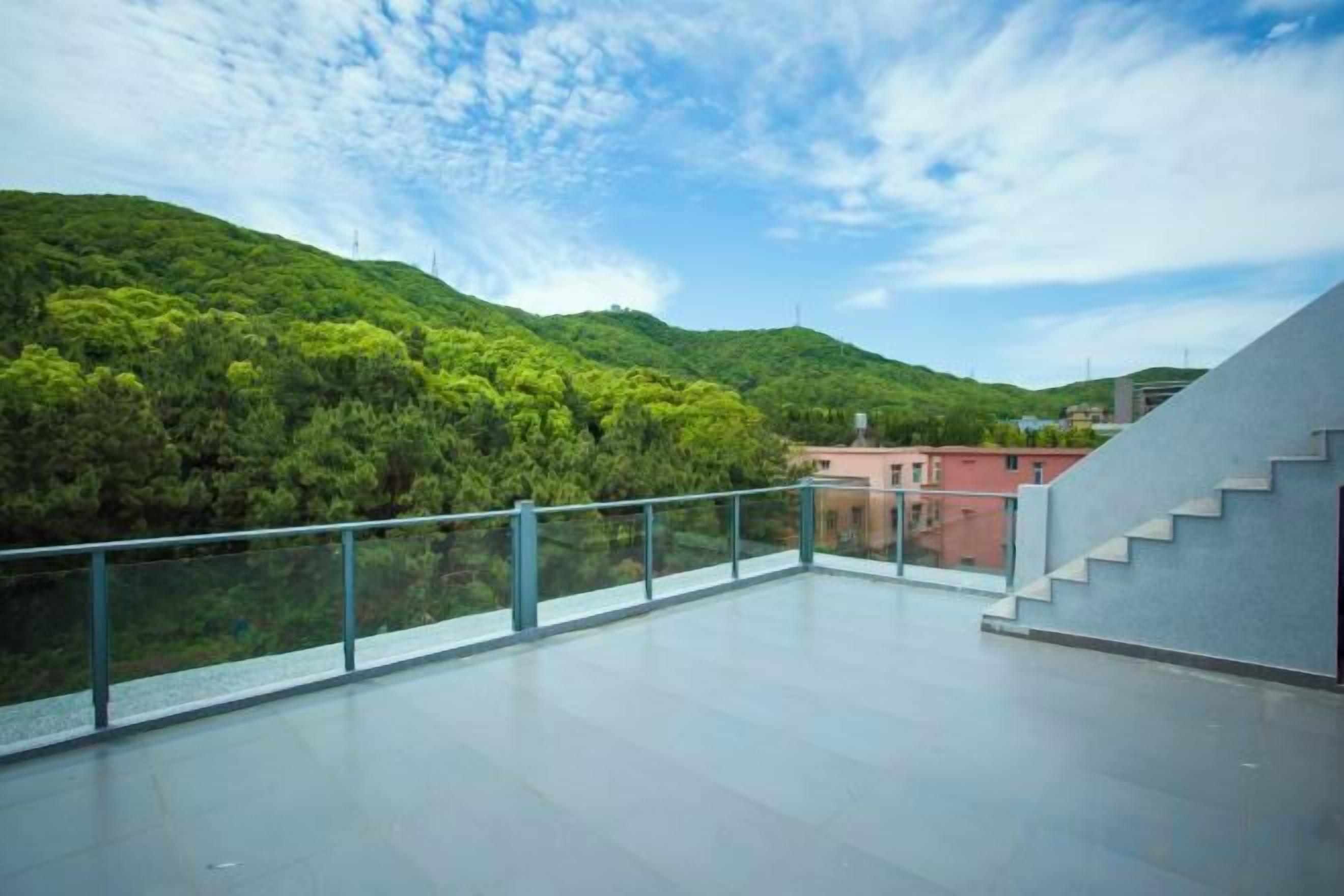 A modern building with a glass balcony overlooking a green hillside.