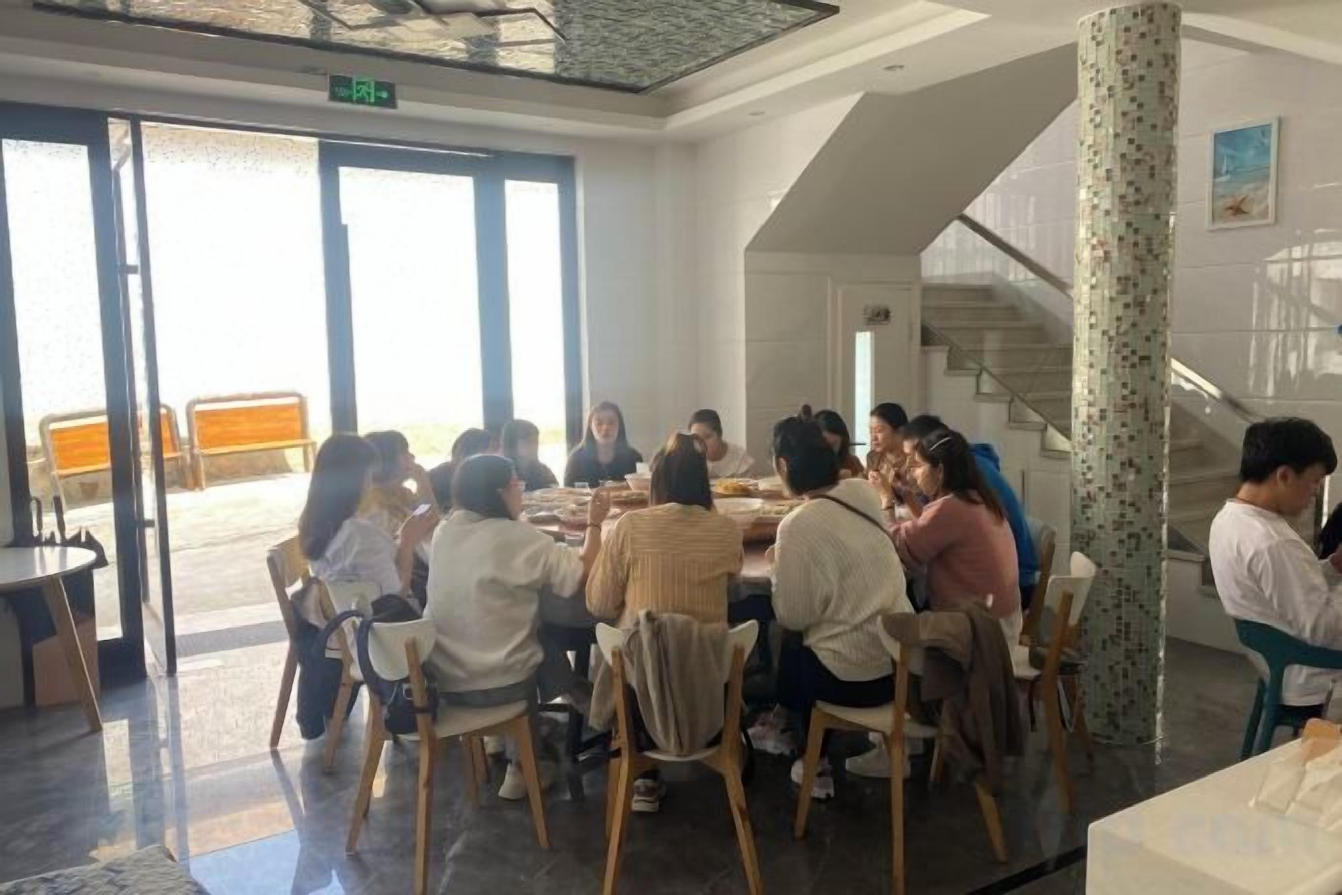 A group of people seated around a table in a room with a staircase and a door leading outside.