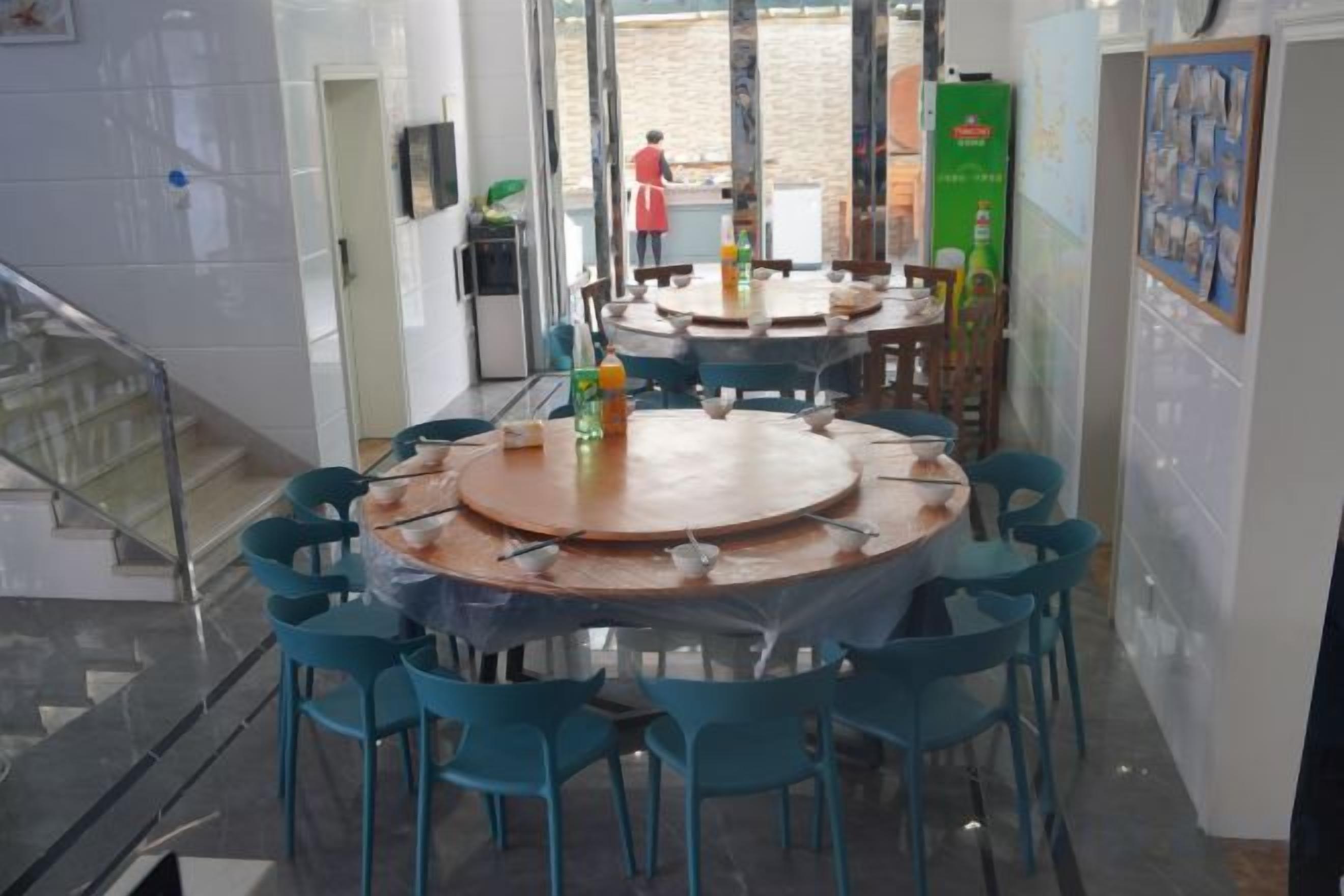 Un comedor con mesas redondas y sillas azules, una escalera y vistas al exterior.