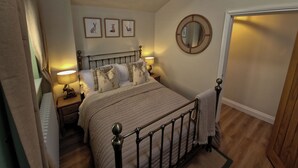 A bedroom with a bed, bedside lamps, a chandelier, framed animal pictures, a mirror, and a door. - High Spec 1-bed Cottage in Staindrop, Darlington (Darlington)