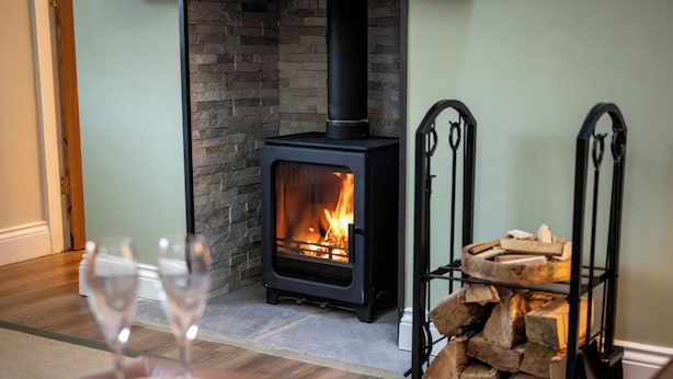 A cozy room with a wood-burning stove, a stack of firewood, and two glasses on a table. - High Spec 1-bed Cottage in Staindrop, Darlington (Darlington)