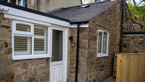 A stone house with a white door and windows, a black gutter, and a wooden fence. - High Spec 1-bed Cottage in Staindrop, Darlington (Darlington)