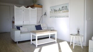 Ein Wohnzimmer mit einem weißen Sofa, einem Couchtisch, einem kleinen weißen Tisch und einem Gemälde an der Wand.