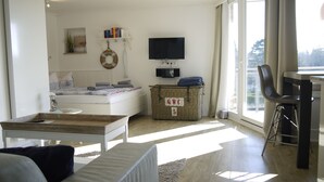 Ein geräumiges Wohnzimmer mit einer Couch, einem Holztisch, einem Fernseher und einem Korbwäschesessel.