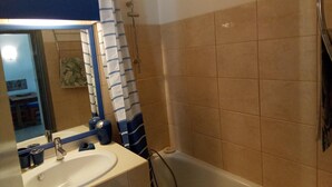 A bathroom with a white sink, blue-striped shower curtain, and beige tiled walls. - Au Port,agreable Appartement de Plain Pied Avec Terrasse (Hourtin)