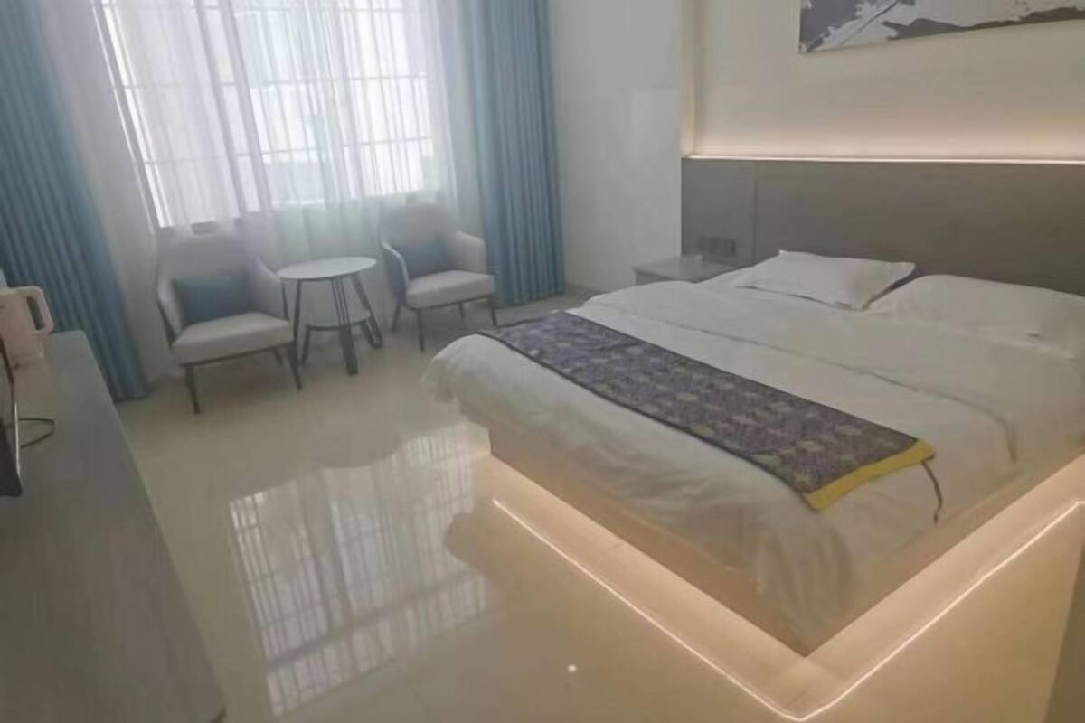 A hotel room with a bed, a small table, two chairs, and a window with curtains.